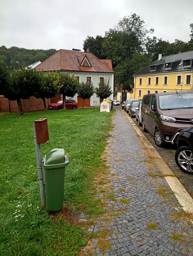 Z podélného parkování udělat kolmé a dosadit dva velké stromy a třeba nějaký umělecký prvek.